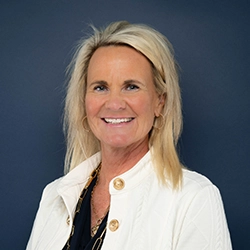 Kristen Trovas smiles into the camera against a dark blue background.